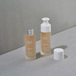 Last inn bildet i Galleri-visningsprogrammet, To flasker med "Hydrate Elixir" på en grå overflate, en med og en uten pumpetopp.
