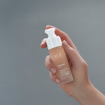 Last inn bildet i Galleri-visningsprogrammet, Flaske med Hudpleieprodukt "Hydrate Elixir" holdt i en hånd mot grå bakgrunn.
